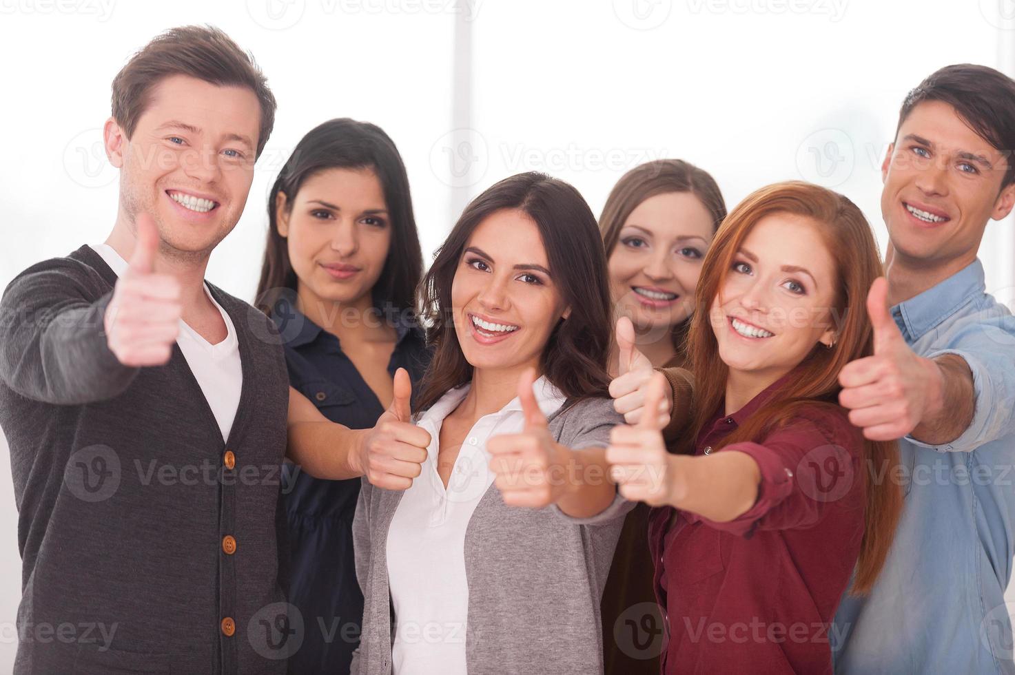 somos un grupo de equipo exitoso de jóvenes alegres parados uno cerca del otro y gesticulando foto