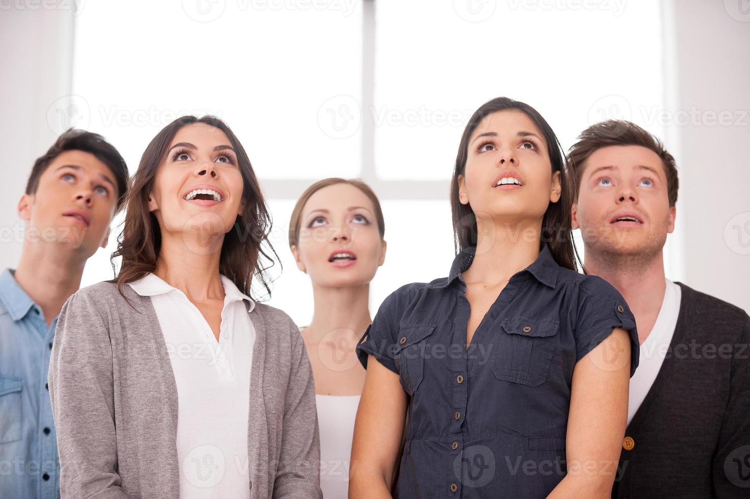 What is that Surprised group of young people looking up while standing close to each other photo