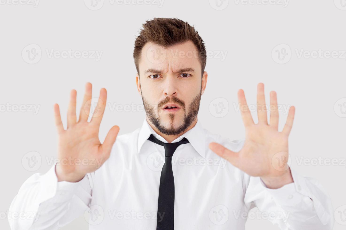 Stop Serious young man in shirt and tie holding his hands outstretched while standing against grey background photo