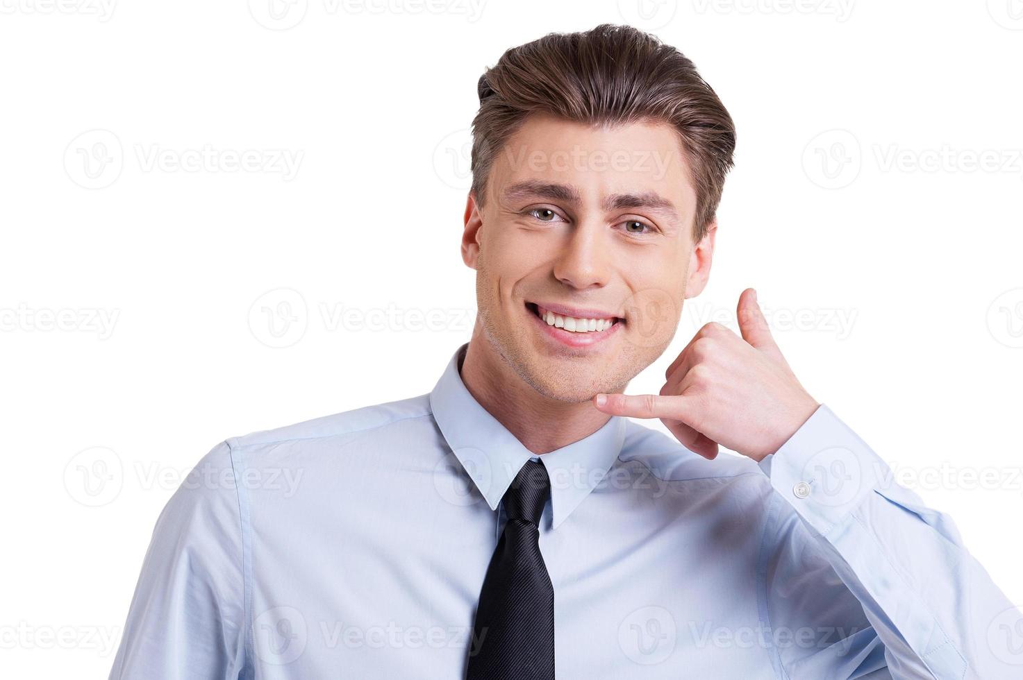 Waiting for your call Handsome young man in formalwear gesturing telephone sign and smiling while standing isolated on white photo