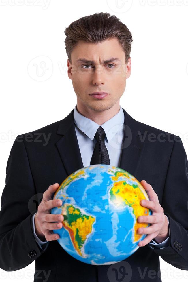 The world is mine Confident young man in formalwear holding globe and looking at camera while standing isolated on white photo