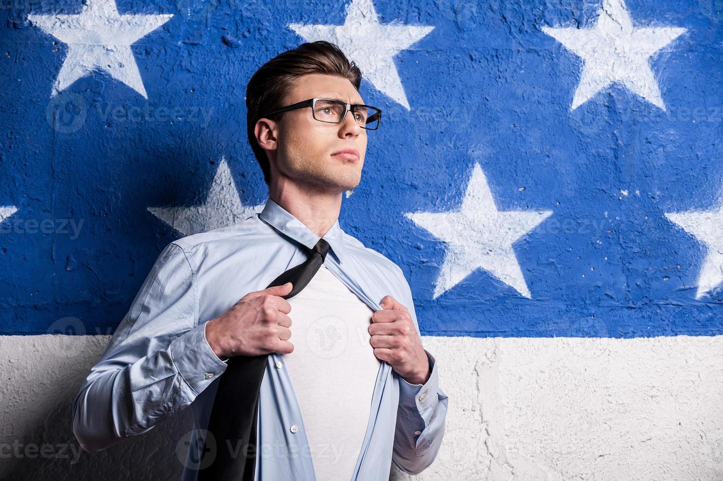 Ready to save the world. Confident young man in formalwear undressing his shirt and looking away while standing against background photo