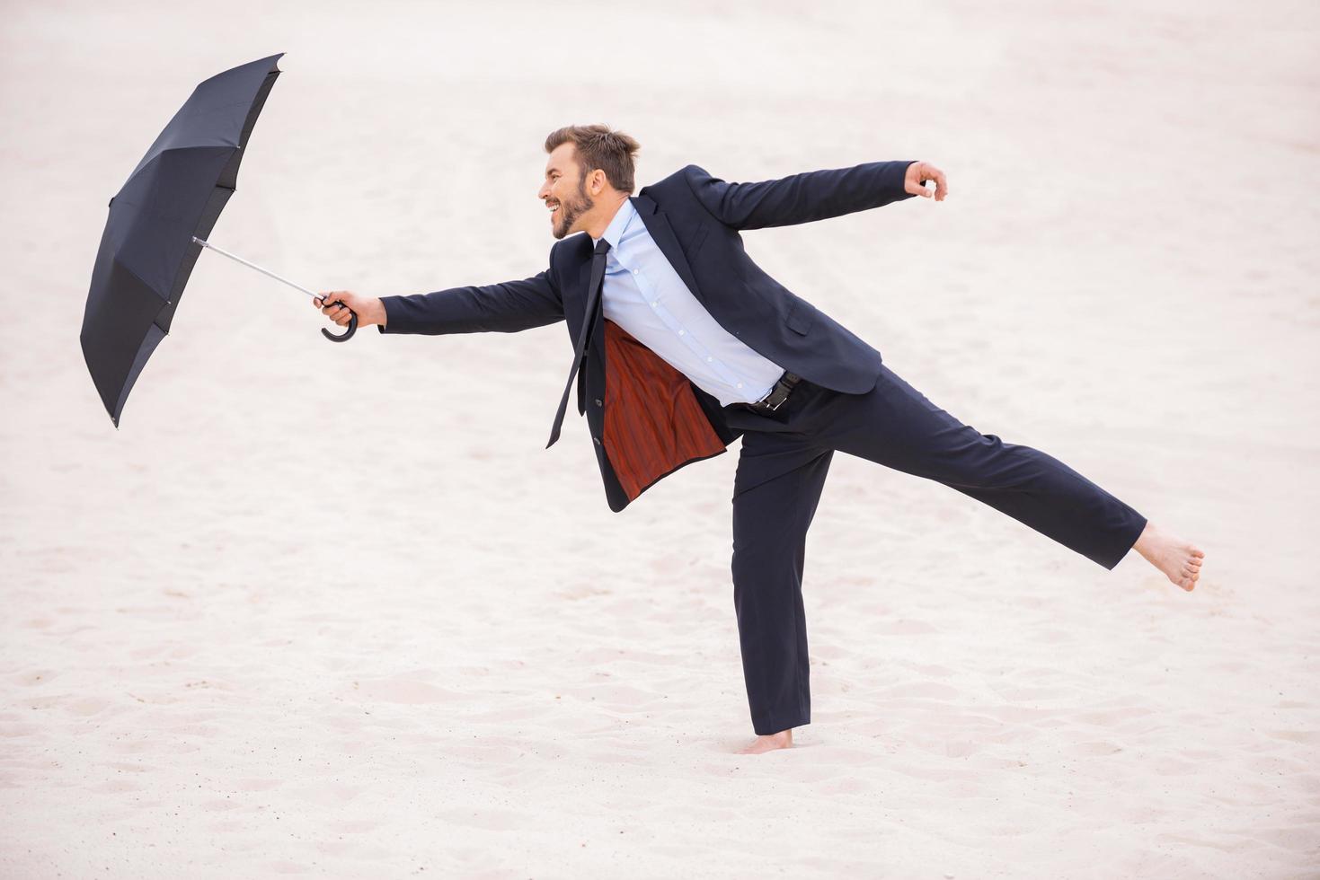 Gentleman with umbrella. Playful young man in formalwear holding umbrella while standing in desert photo