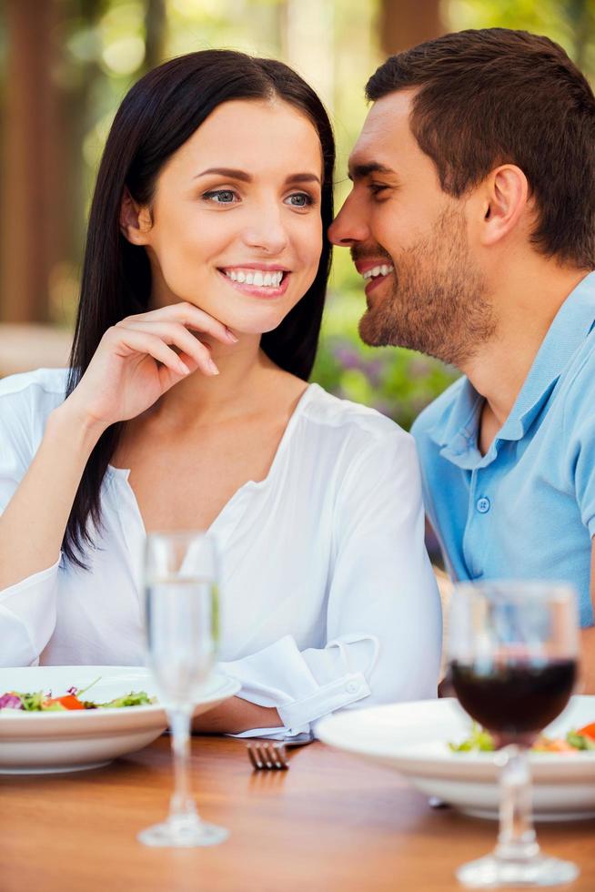 Tender words for her. Handsome young man telling something to his girlfriend and smiling while relaxing in outdoors restaurant together photo