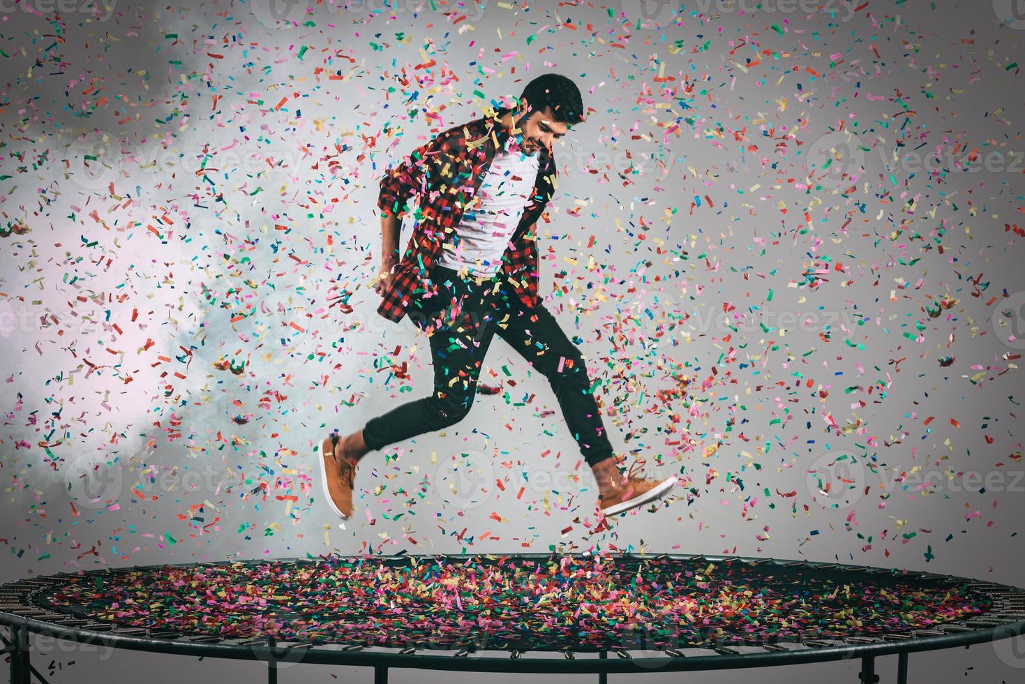 Mid-air fun. Mid-air shot of handsome young man jumping on trampoline with confetti all around him photo