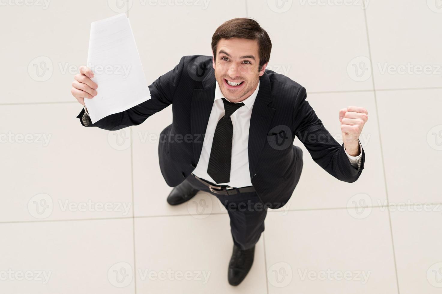 This contract is mine Top view of excited young man in formalwear holding a paper in one hand and gesturing photo