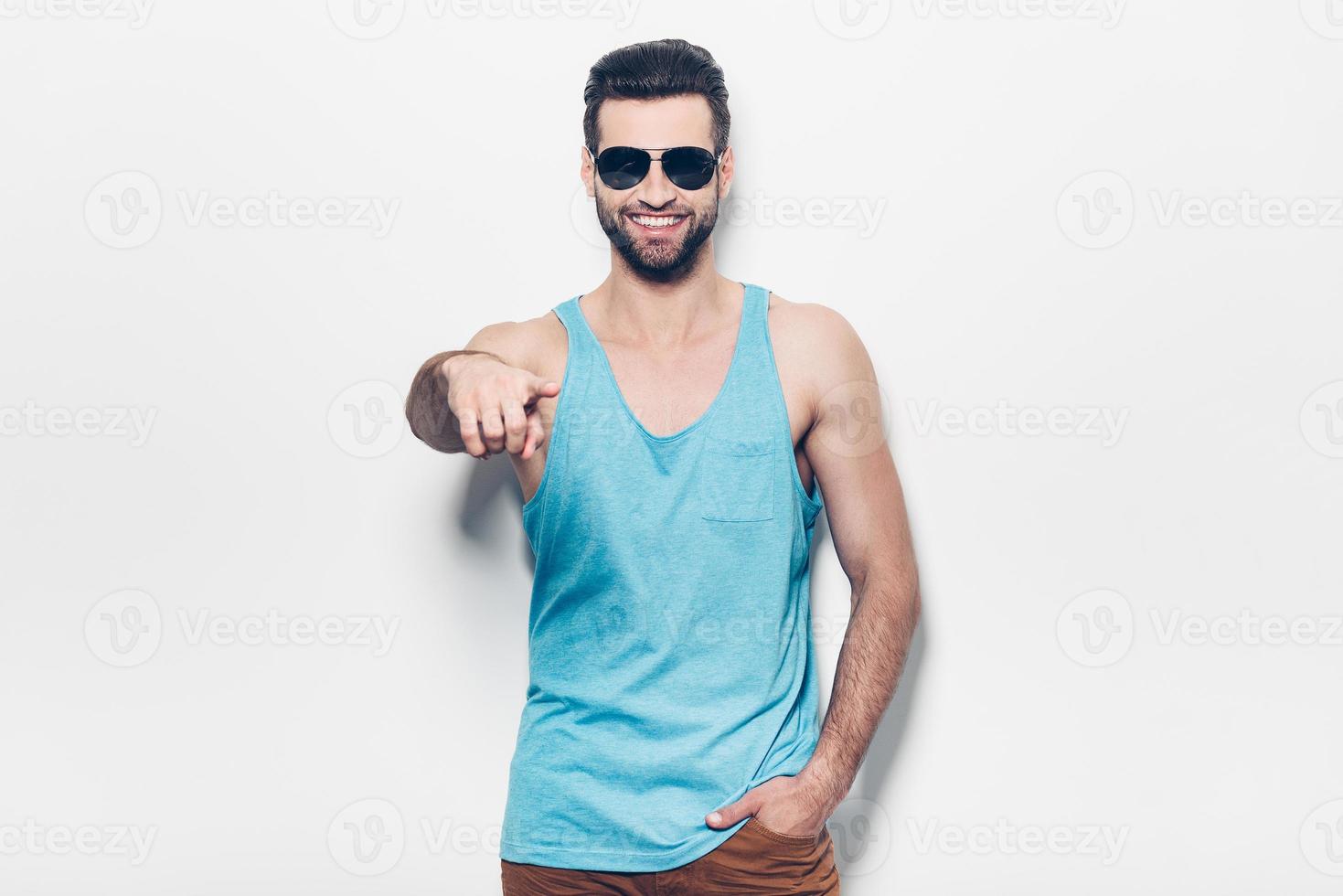 Choosing you. Confident young handsome man in sunglasses pointing you and smiling while standing against white background photo