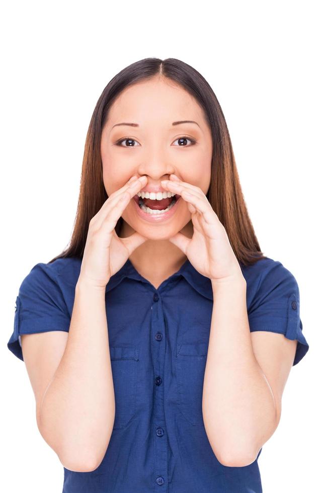 Telling the great news. Attractive young Asian woman shouting and holding hand near mouth while standing isolated on white photo