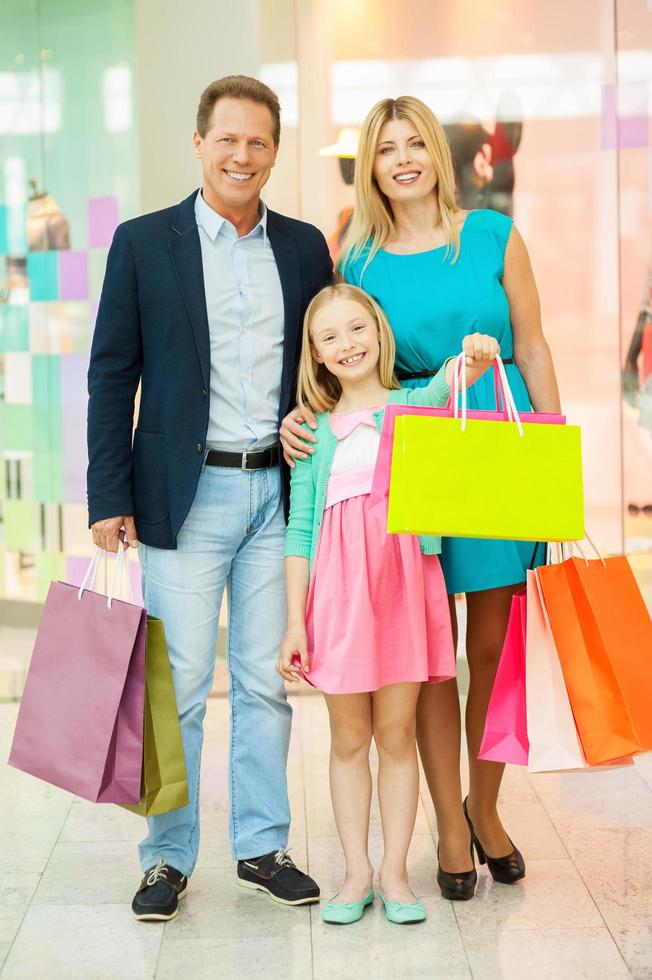 familia en centro comercial. longitud completa de familia alegre sosteniendo bolsas de compras y sonriendo mientras está de pie en el centro comercial foto