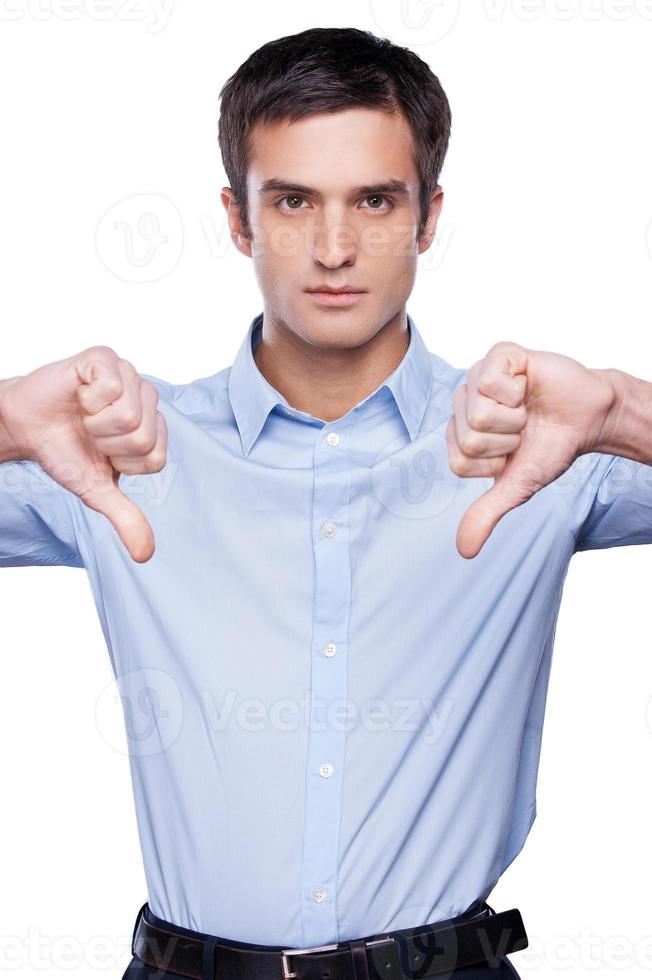 Rejected Serious young man in blue shirt showing his thumbs down and looking at camera while standing isolated on white photo