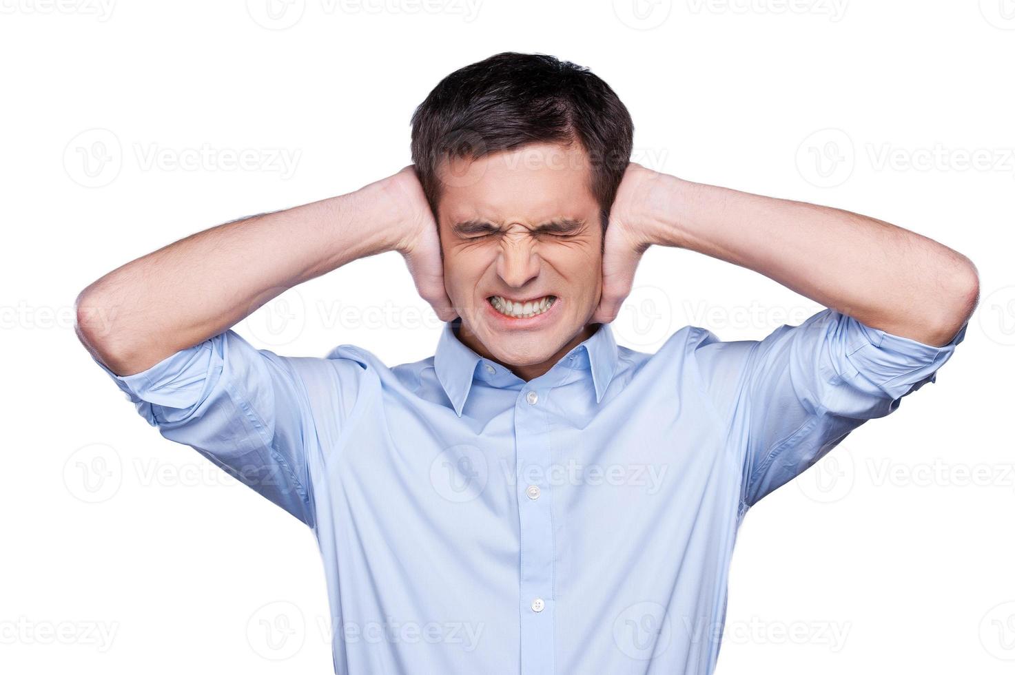 Too loud Handsome young man in blue shirt covering ears with hands and grimacing while standing isolated on white photo