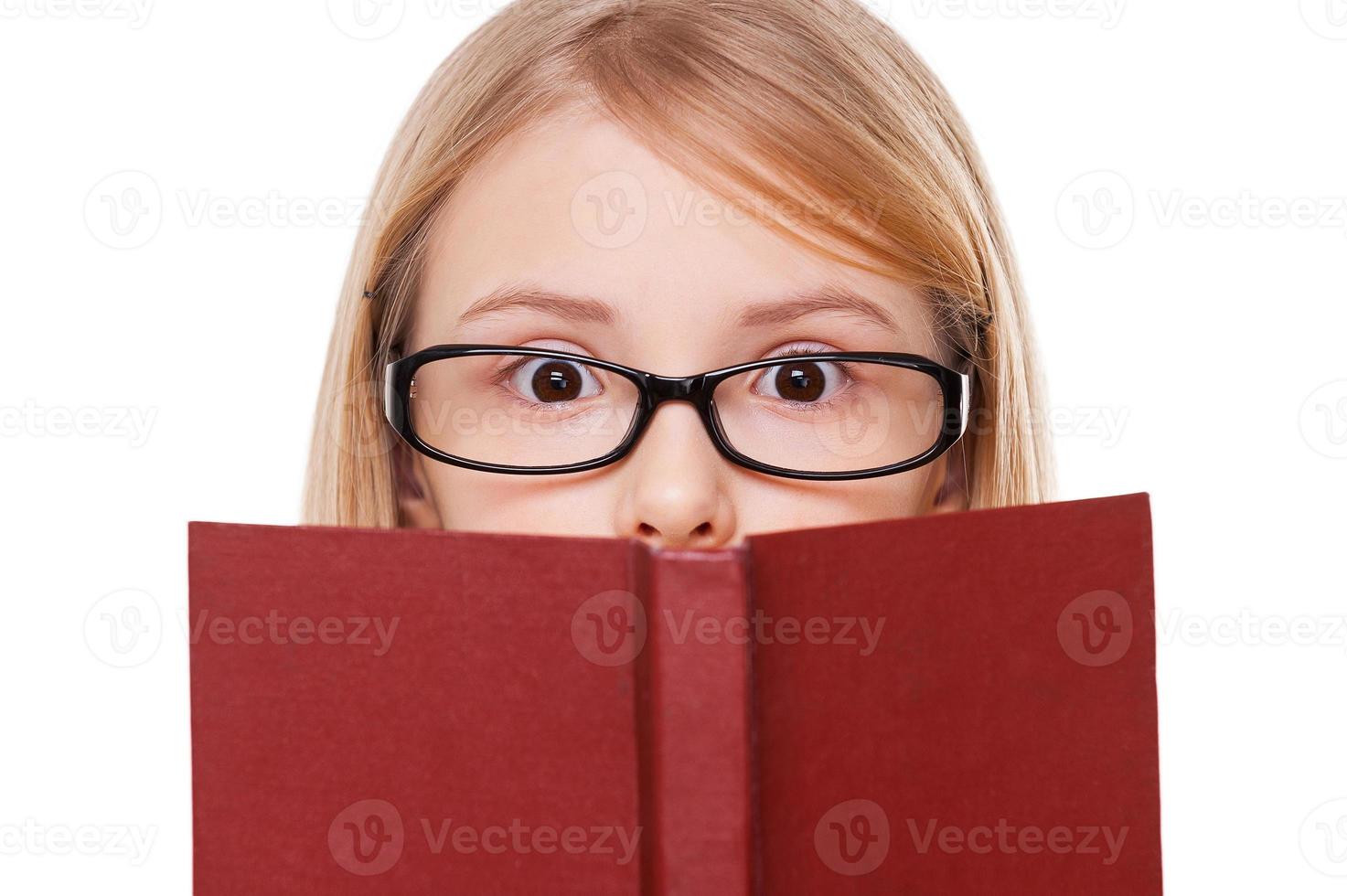 de ninguna manera sorprendió a una niña leyendo un libro y manteniendo la boca abierta mientras estaba aislada en blanco foto