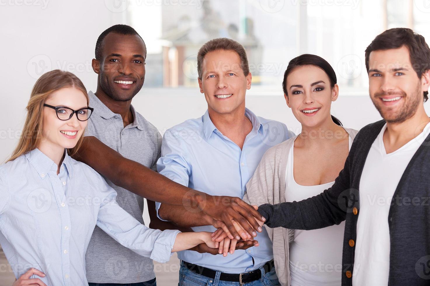 Together we are stronger Group of cheerful business people in casual wear standing close to each other and holding hands together photo