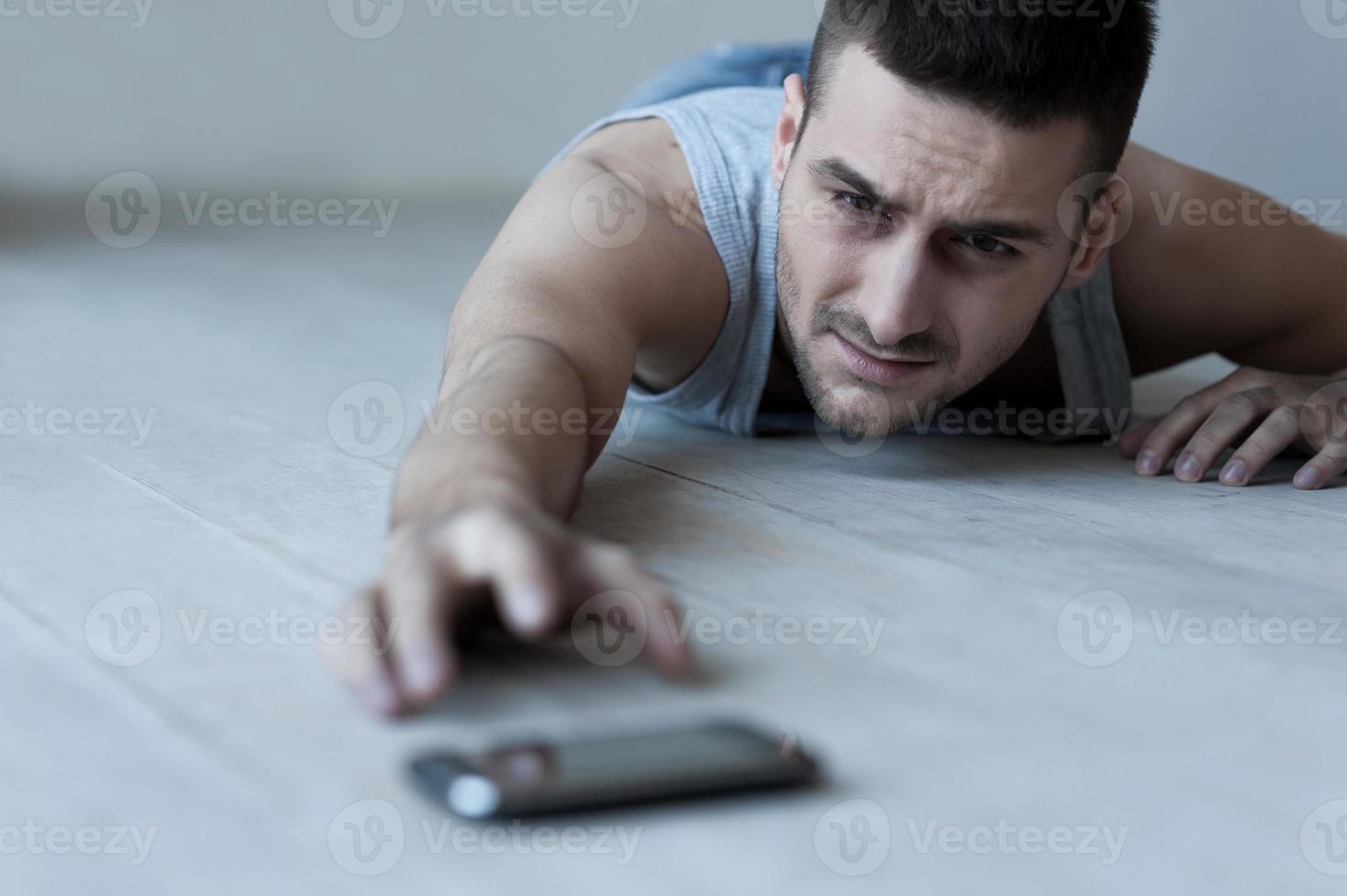 I need help Frustrated young man lying on the floor and stretching hand to the mobile phone photo