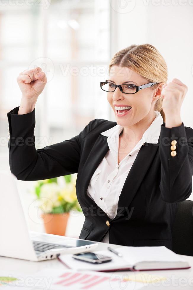 qué día de suerte feliz mujer de negocios madura sentada en su lugar de trabajo y gesticulando foto