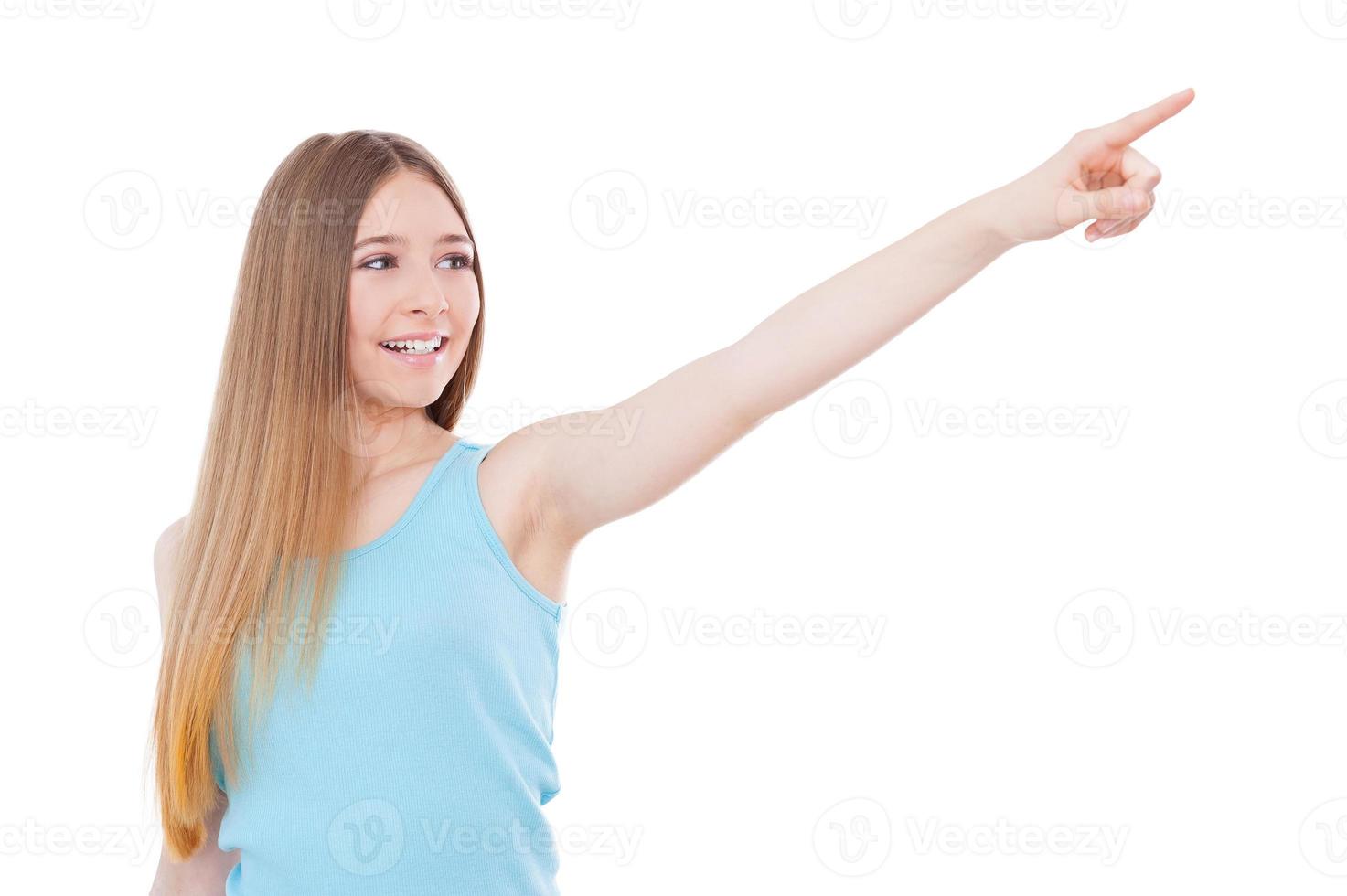 Just look over there Happy teenage girl pointing away and smiling while standing isolated on white photo