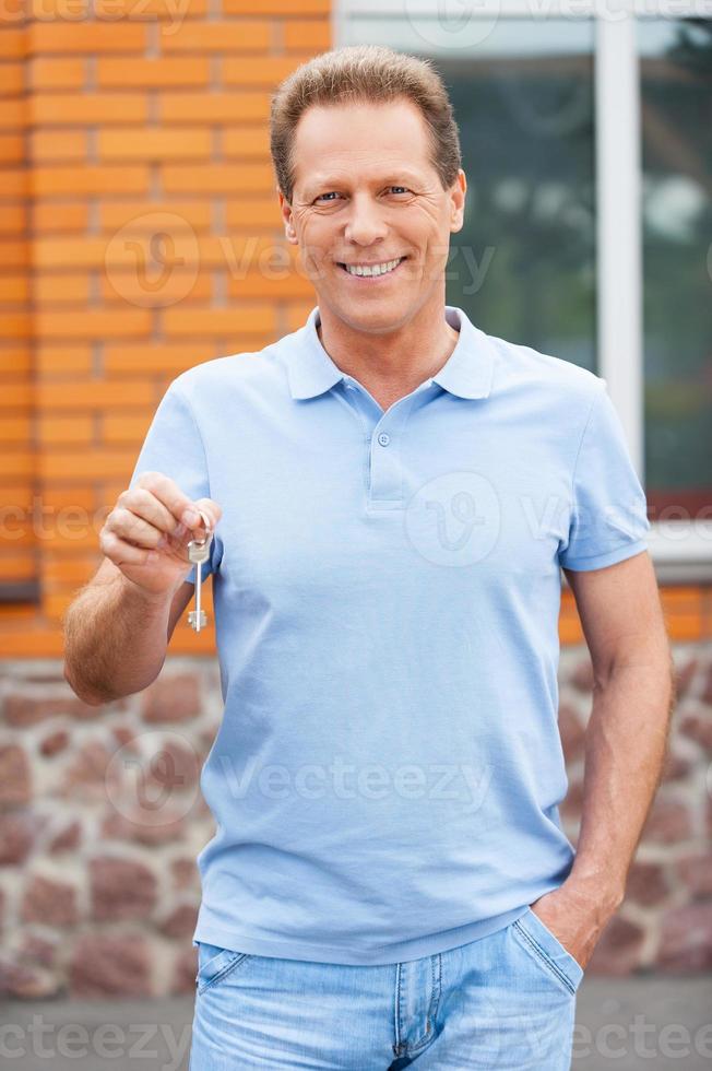 My new house. Handsome mature man standing in front of a house holding a key photo