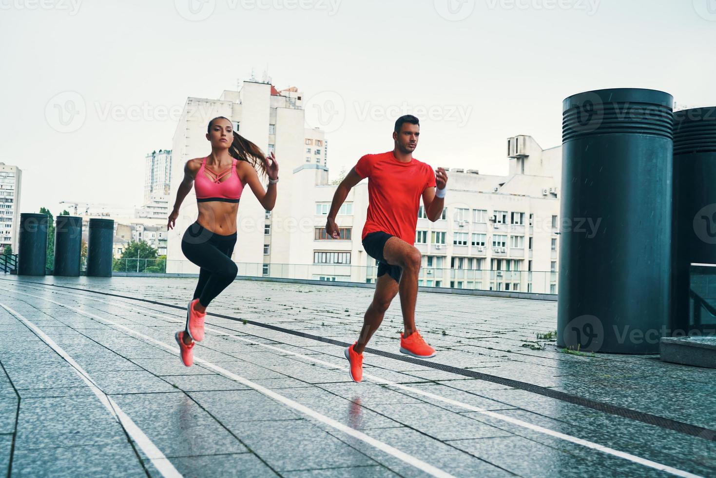 Longitud total de dos jóvenes con ropa deportiva saltando y trotando mientras hacen ejercicio en la calle de la ciudad al aire libre foto