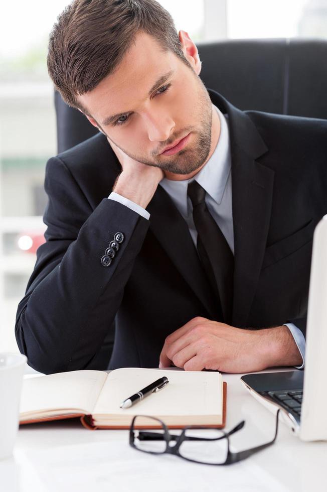 Tired businessman. Frustrated young man in formalwear looking away and touching his neck with hand while sitting at his working place photo