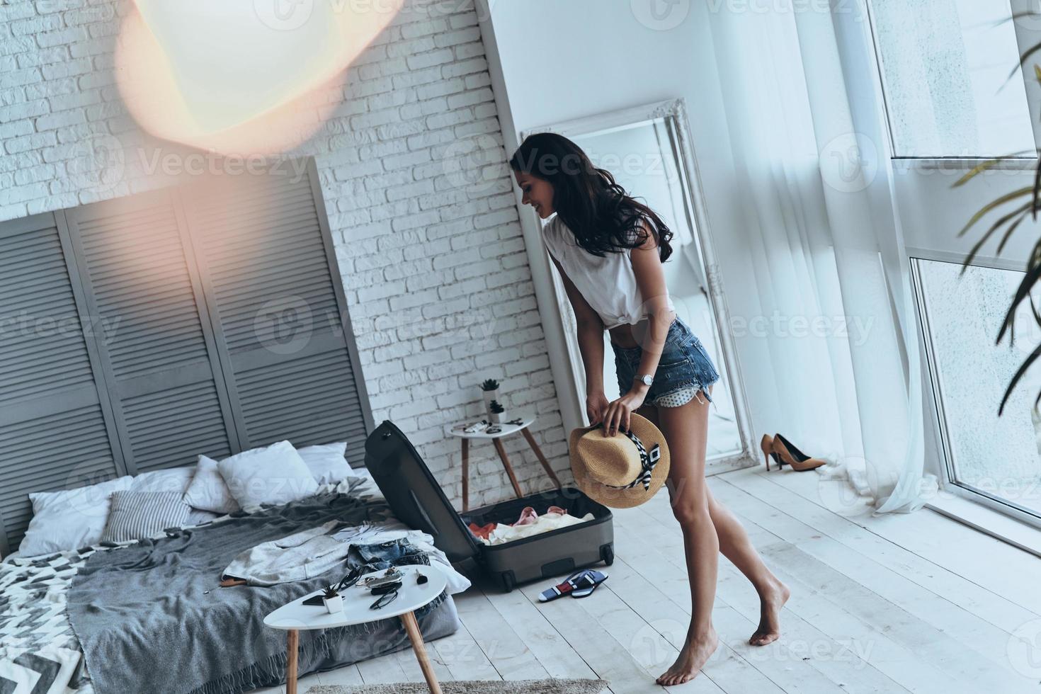 Getting ready for summer vacation. Full length of beautiful young woman holding sun hat while walking in the bedroom photo