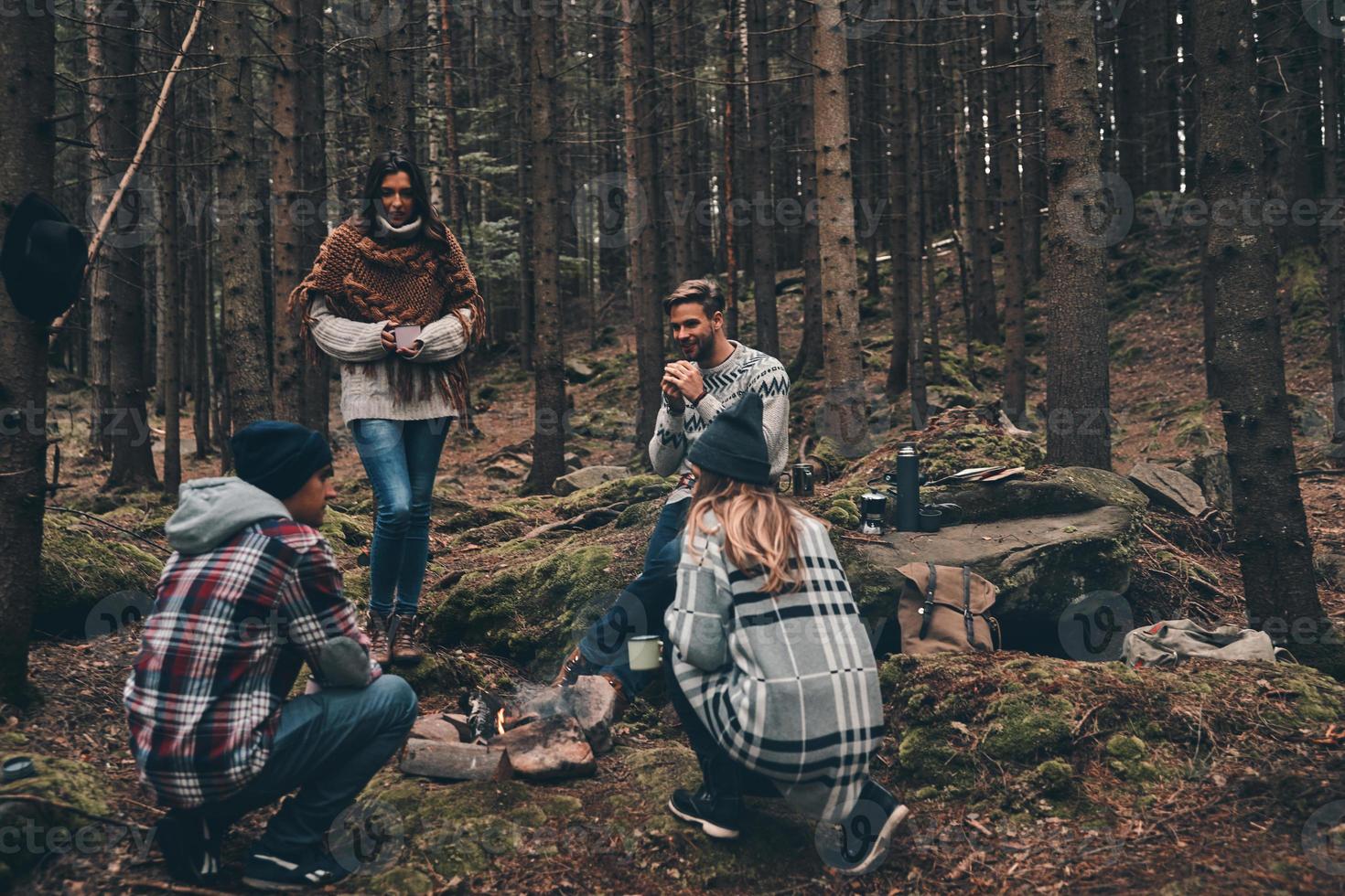 amigos íntimos. grupo de jóvenes felices parados alrededor de la fogata mientras caminan por el bosque foto