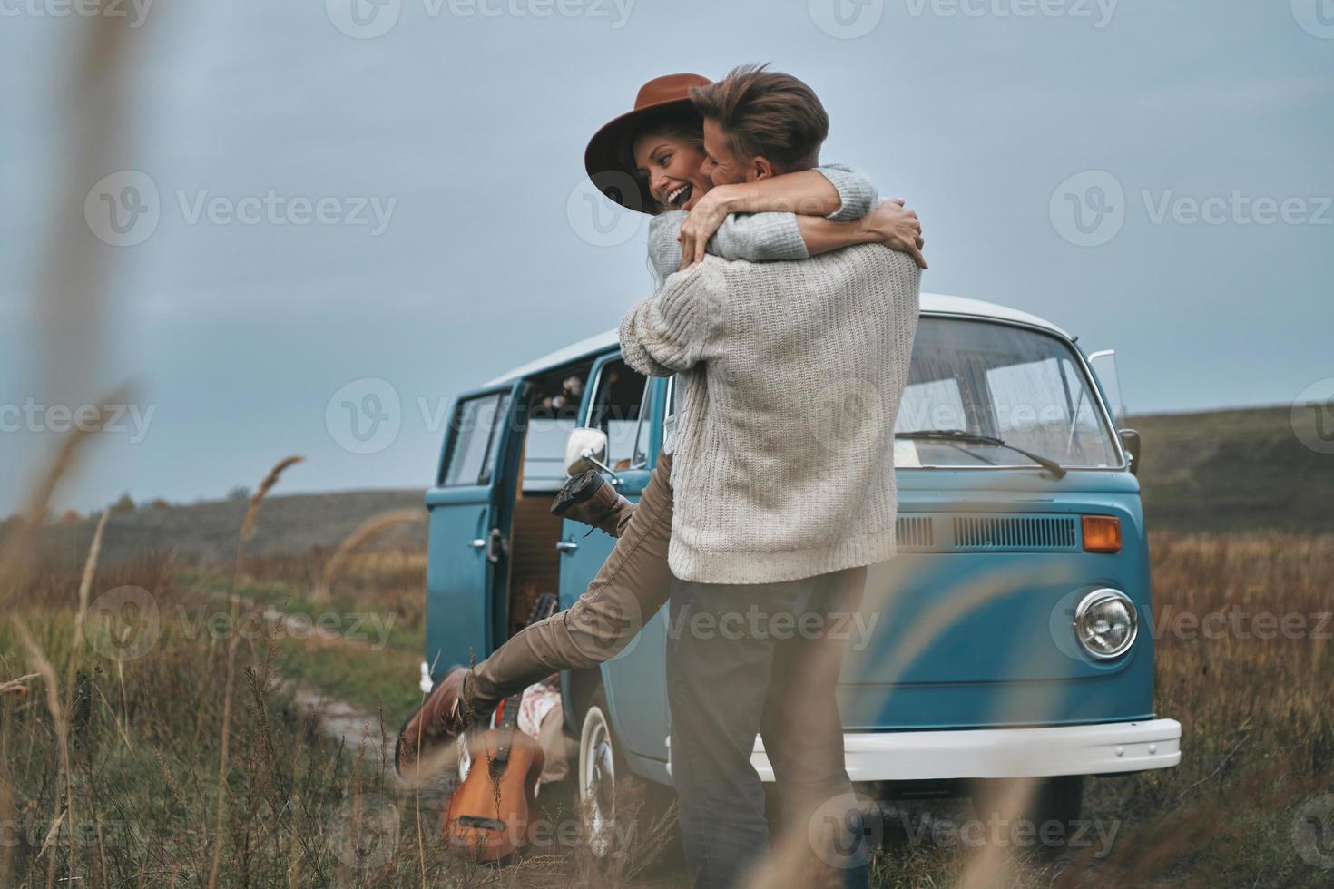 Happy to be around.  Beautiful young couple embracing and smiling while standing near the blue retro style mini van photo