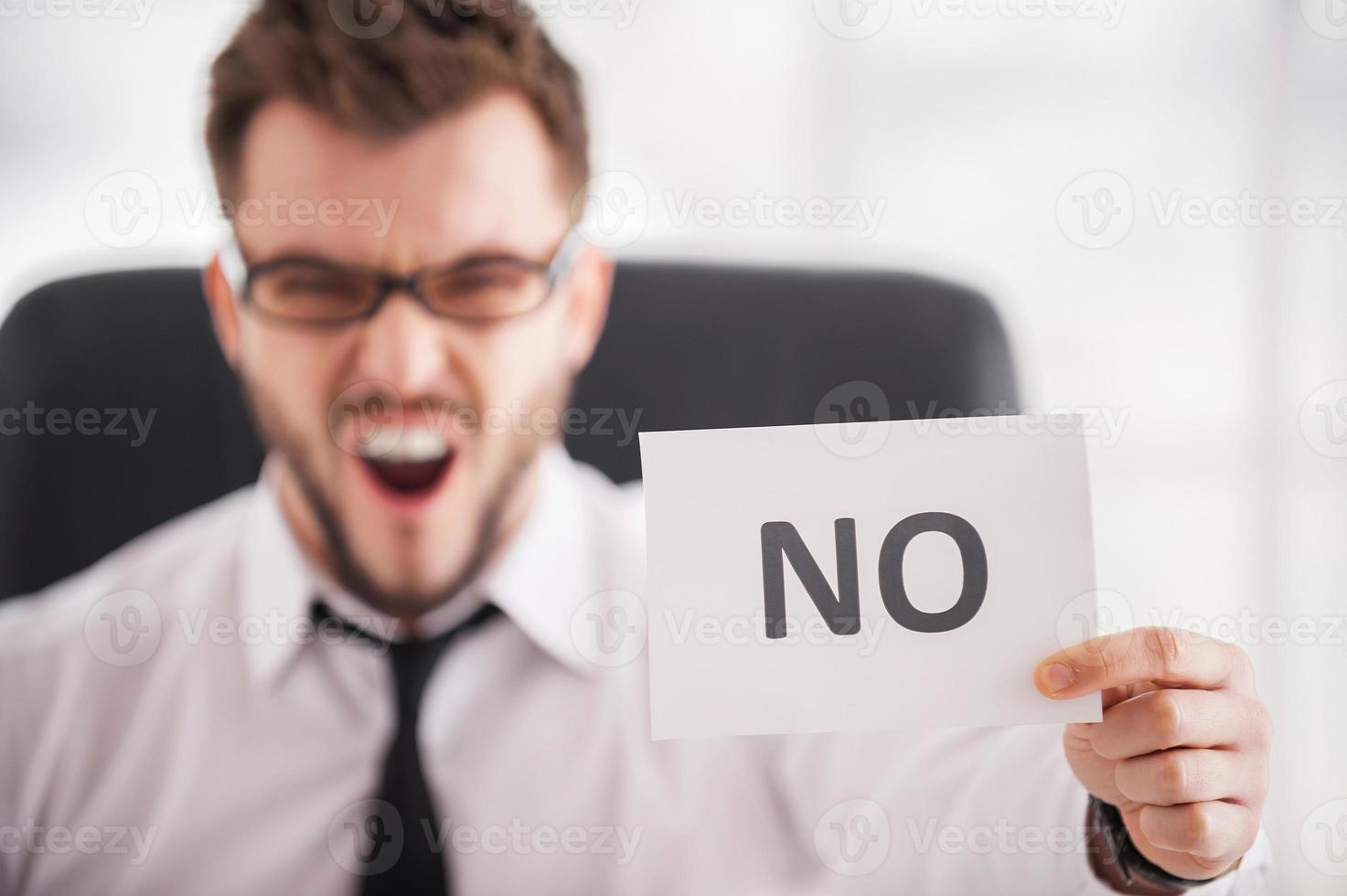 Strict verdict. Furious young man in shirt and tie touching his temple with finger gun and keeping eyes closed while sitting at his working place photo