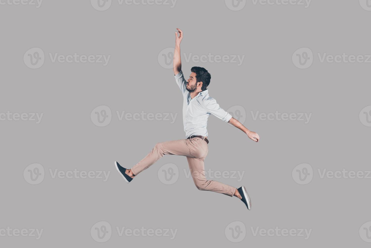 Free jumping. Mid-air shot of handsome young man jumping and gesturing against background photo