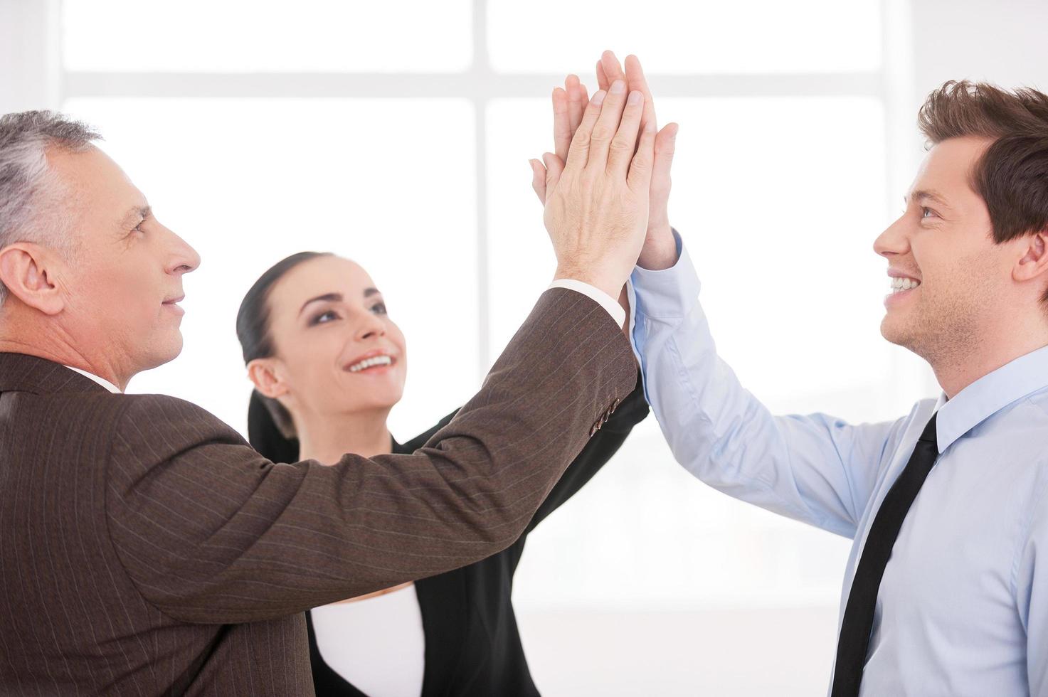 Together we are strong. Three cheerful business people keeping their hands clasped and smiling while standing close to each other photo