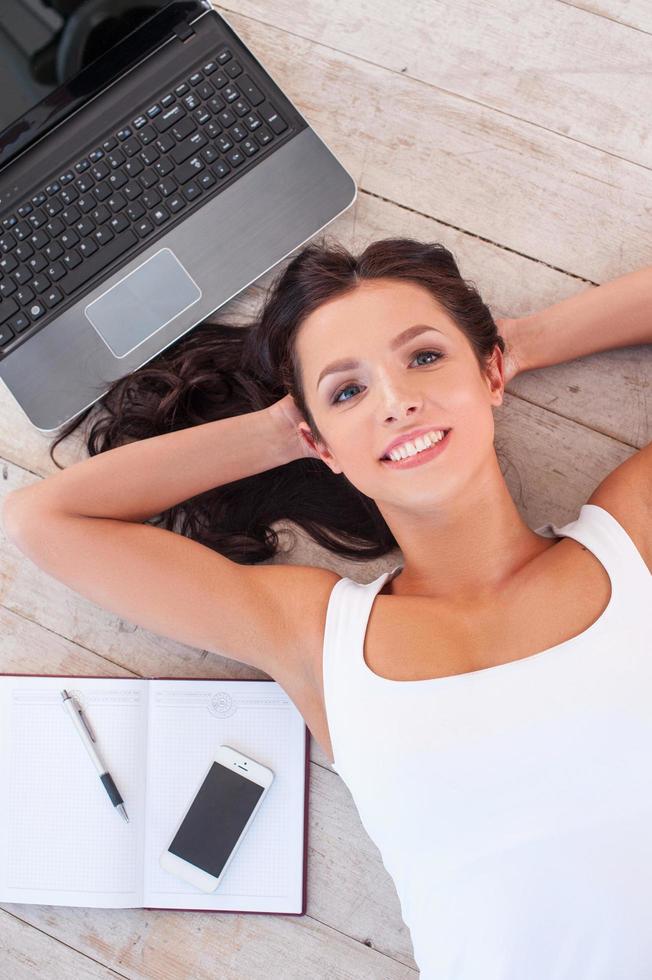 trabajando en la computadora. vista superior de una hermosa joven tendida en el suelo con computadora y teléfono móvil foto