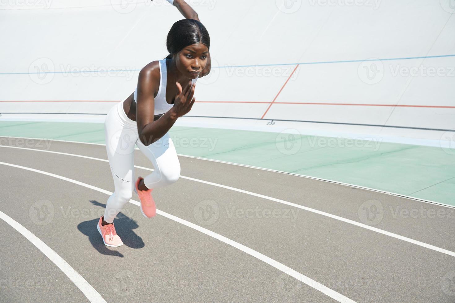 Beautiful young African woman in sports clothing running on track outdoors photo