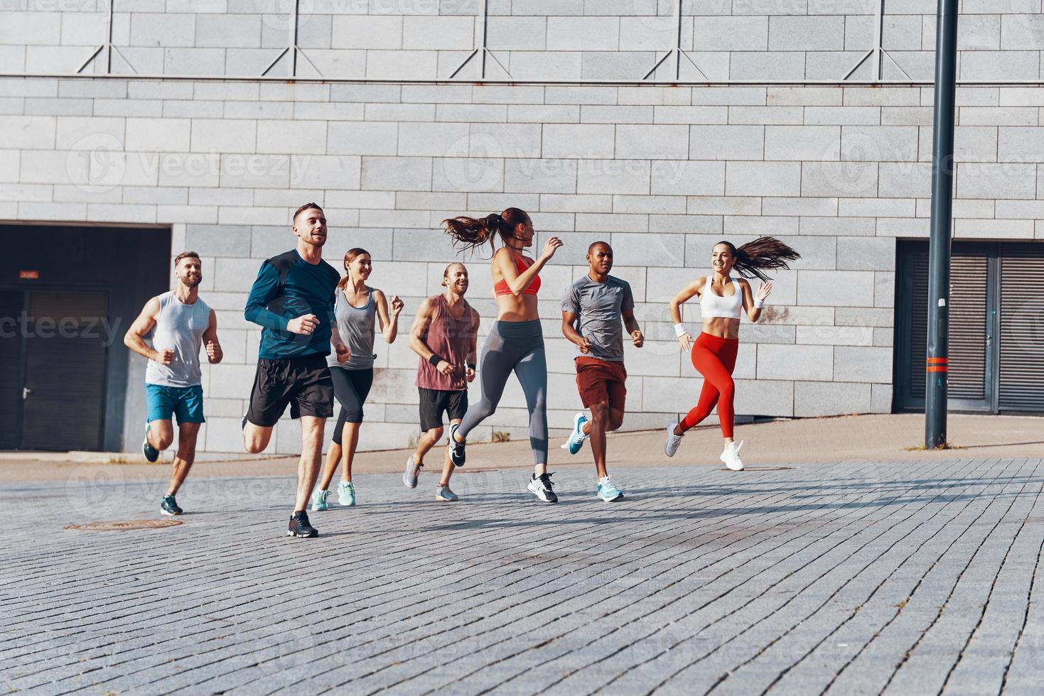 toda la longitud de los jóvenes en ropa deportiva trotando mientras hacen ejercicio al aire libre foto