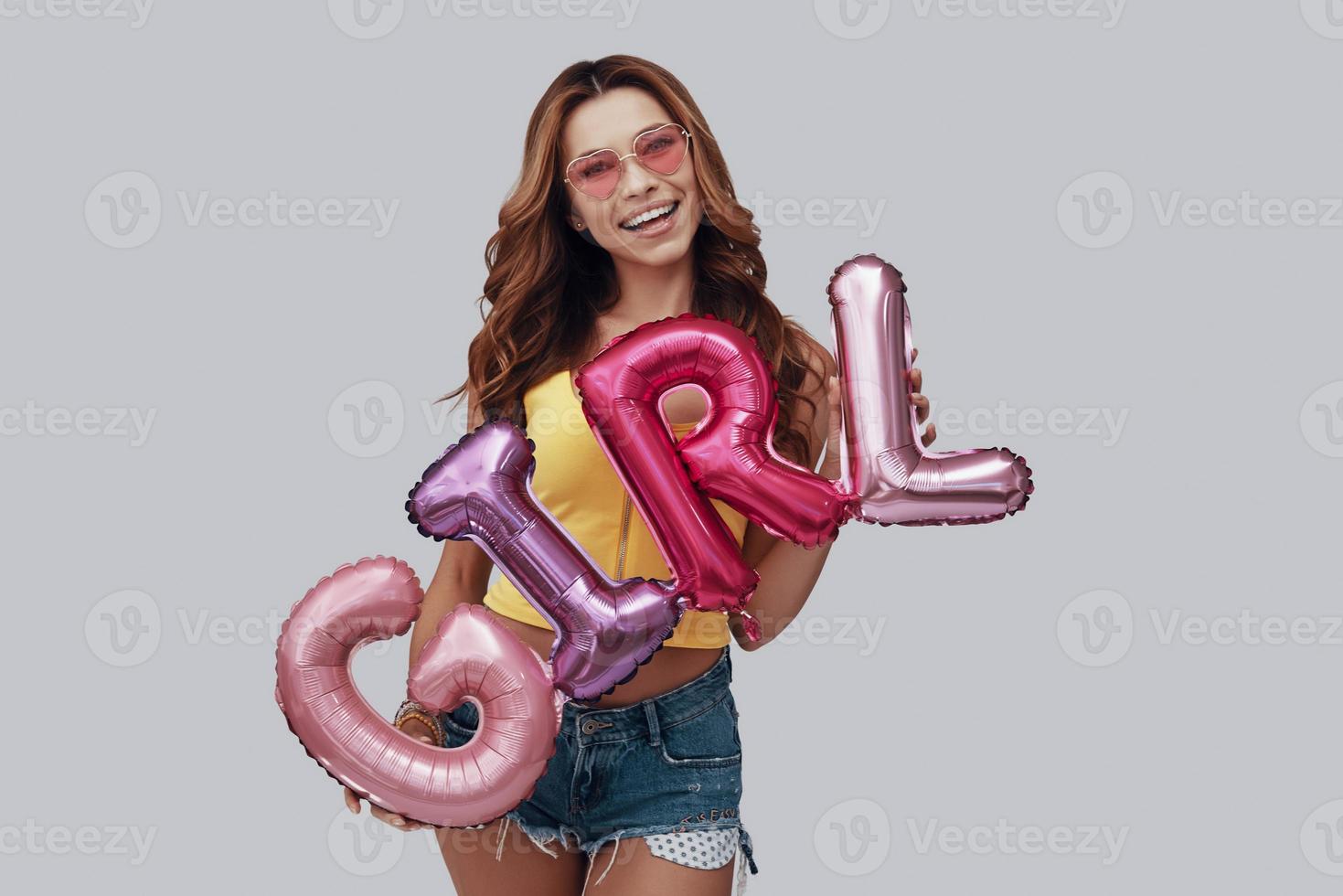 Attractive young woman looking at camera and smiling while standing against grey background photo