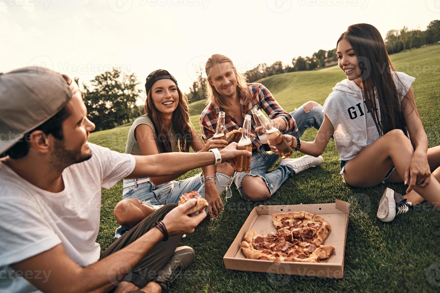 Best weekend ever. Group of young smiling people in casual wear toasting with beer while enjoying picnic outdoors photo