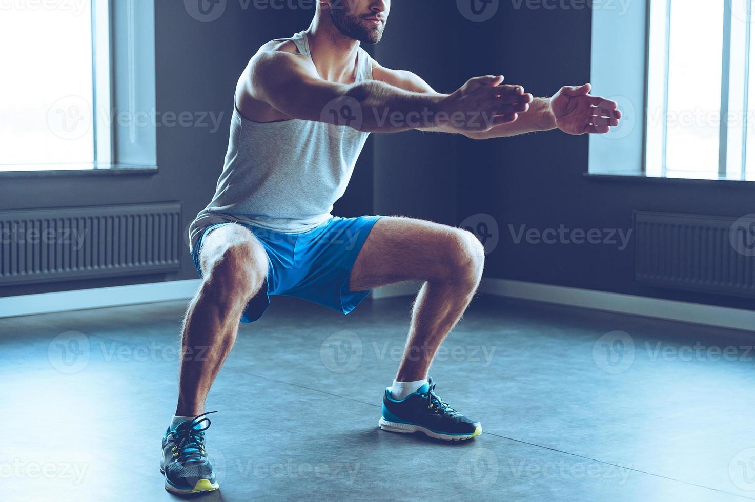 Deep squat. Part of young man in sportswear doing squat at gym photo