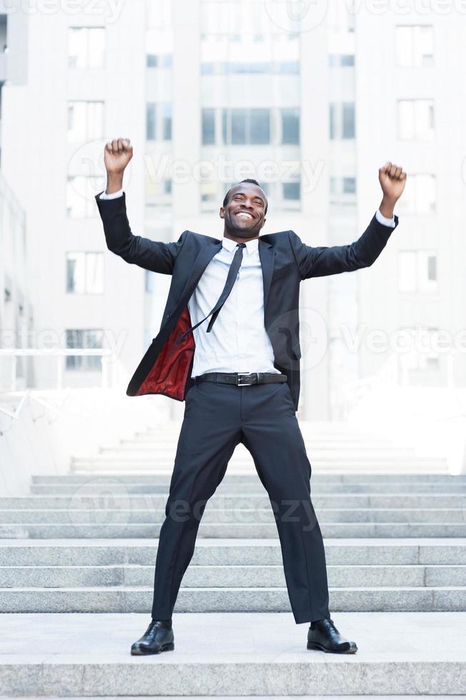 The best day ever Full length of happy young African man in formalwear keeping arms raised and expressing positivity while standing outdoors photo