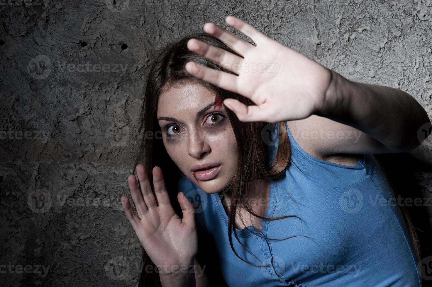 Please no Terrified young woman looking at camera and stretching out hand while leaning at the dark wall photo