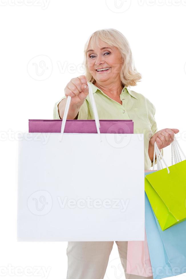 Shopping is my hobby Happy senior woman stretching out hand with shopping bags and smiling while standing isolated on white background photo