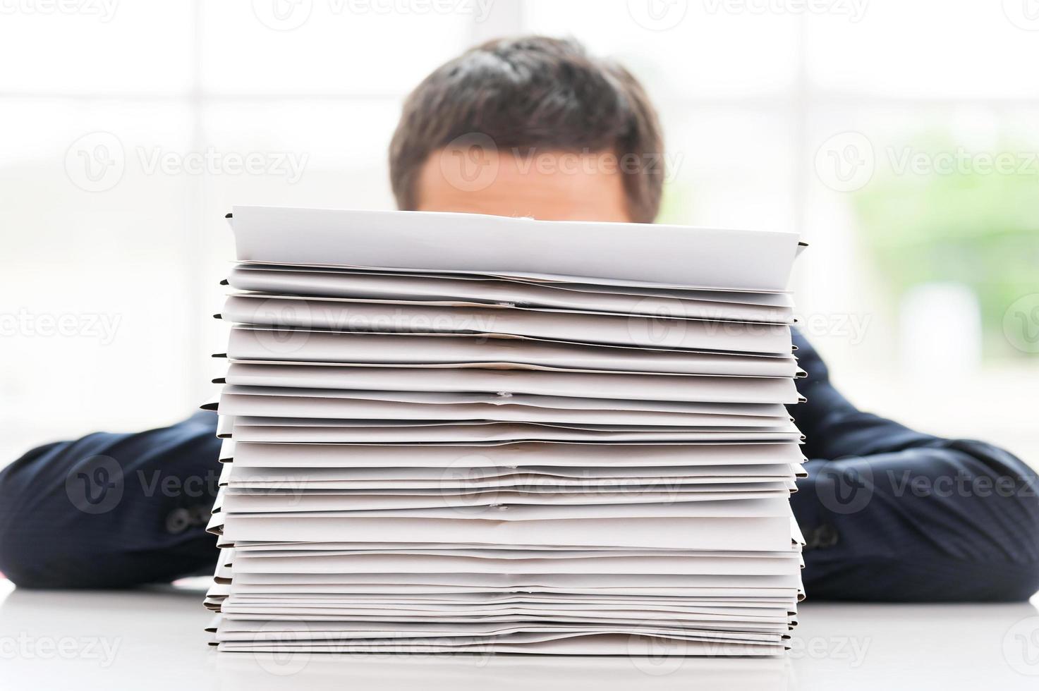 So much work to do Businessman hiding behind a stack of documents laying on the table photo