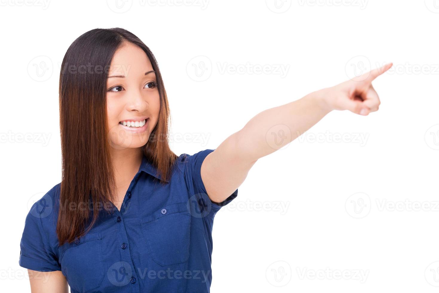 Over there Beautiful young Asian woman pointing away and smiling while standing isolated on white photo