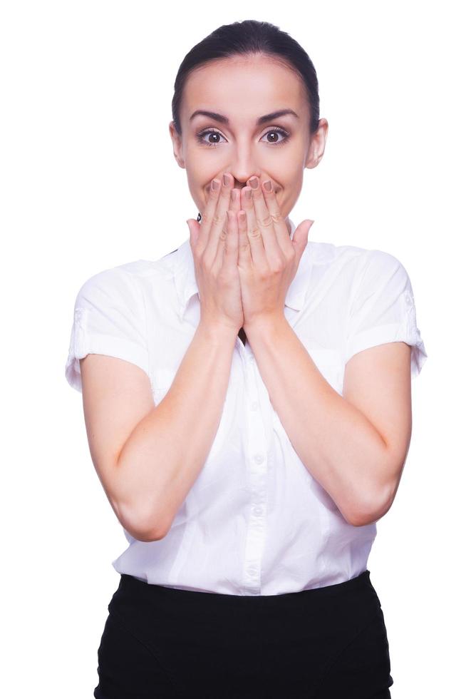 Surprised businesswoman. Surprised young woman in formalwear looking at camera and covering mouth with hands while standing isolated on white photo