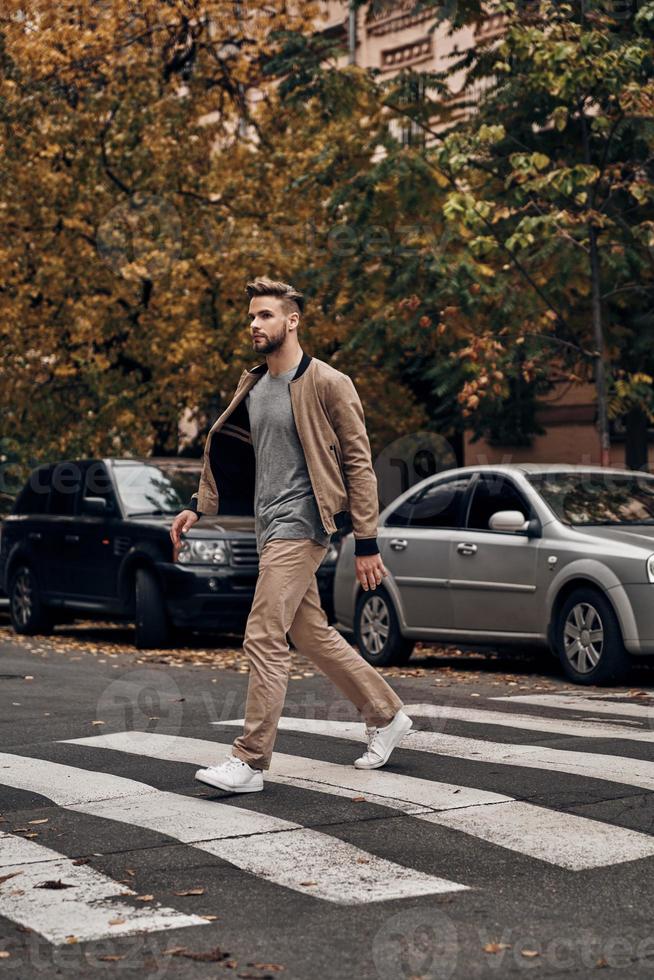 Always careful. Full length of handsome young man in casual wear walking across a zebra crossing while spending time outdoors photo