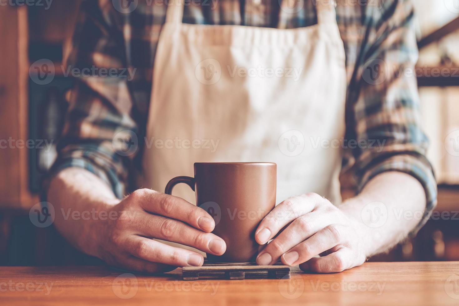 Close-up part of man in apron holding coffee cup while standing at bar counter photo