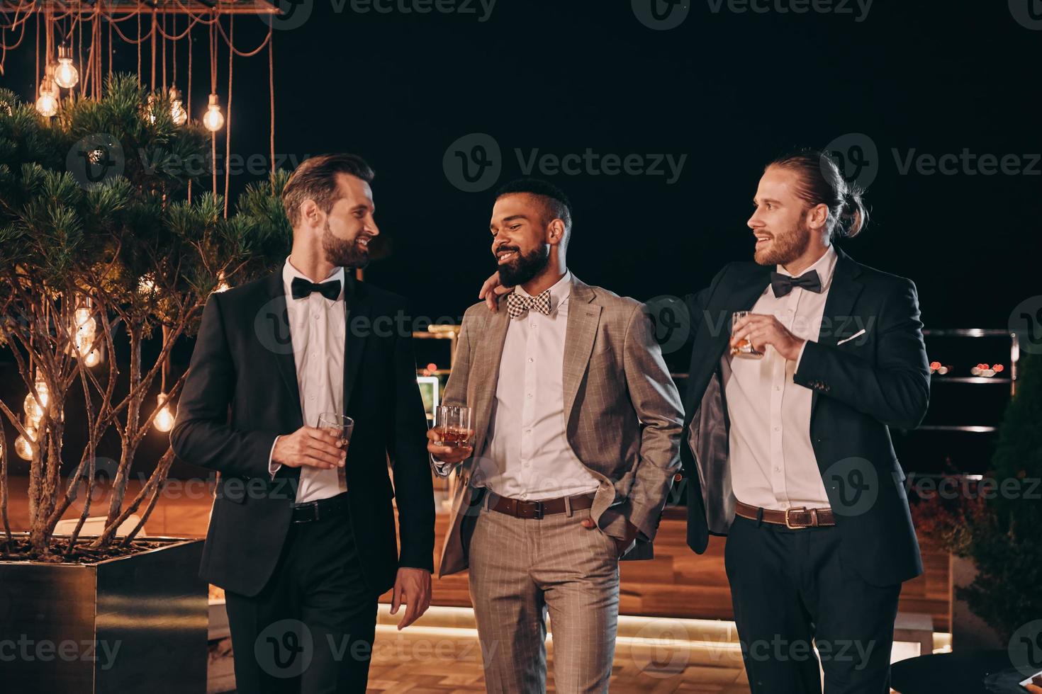 Three handsome men in suits drinking whiskey and communicating while spending time on party photo