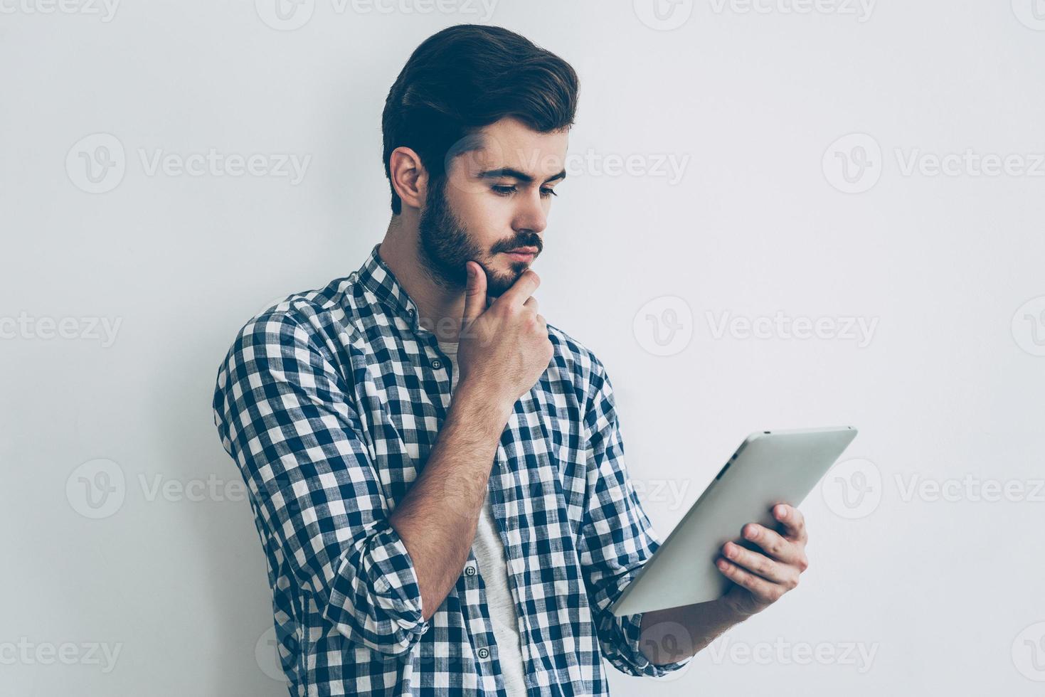 Thinking about solution. Handsome young man holding digital tablet and looking at it photo