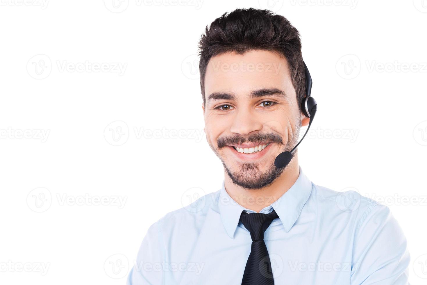 operador masculino confiado. retrato de un apuesto joven operador con auriculares mirando a la cámara y sonriendo mientras se enfrenta a un fondo blanco foto