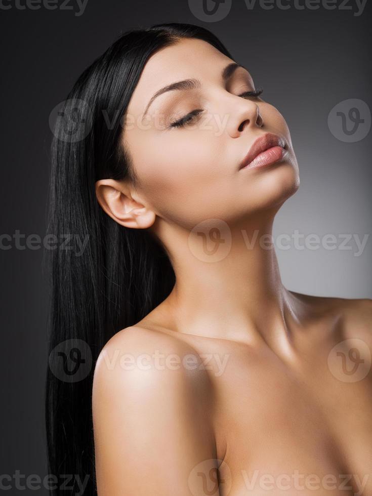 Femininity and tenderness. Beautiful young shirtless woman keeping eyes closed while standing against grey background photo