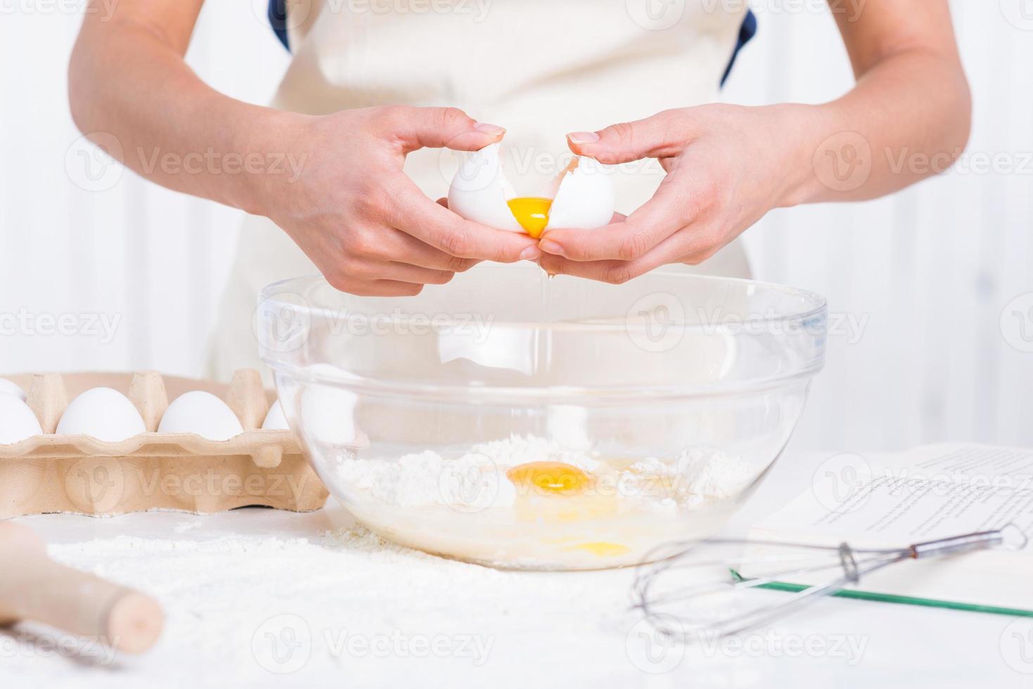 Cracking an egg to a bowl. Close-up of woman cracking egg for pastry photo