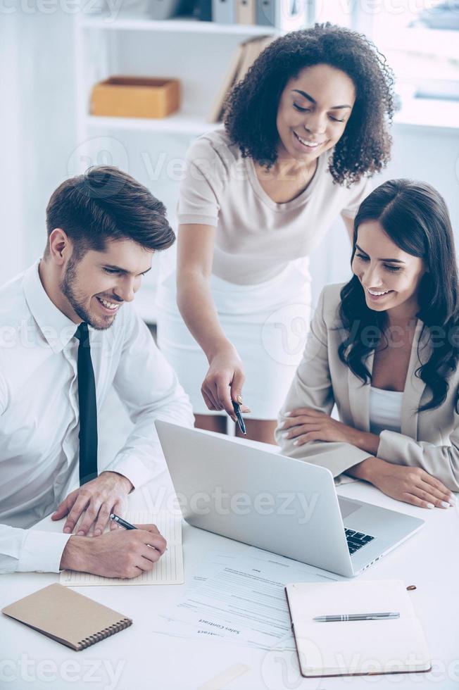 Take a look at this chart Top view of young beautiful African woman pointing at laptop with smile while standing at office with her coworkers photo