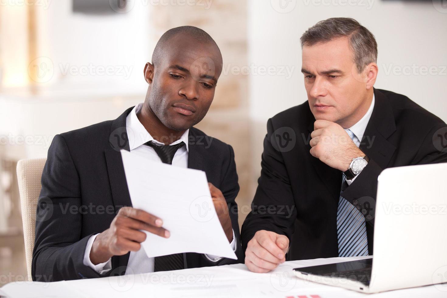 Discussing a project. Two confident business people in formalwear discussing something while one of them pointing a paper photo
